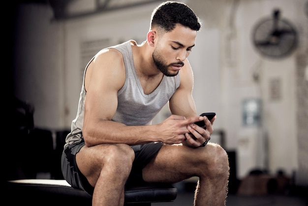 Pausenzeit bedeutet Fitness-Updates Aufnahme eines muskulösen jungen Mannes, der ein Handy in einem Fitnessstudio benutzt