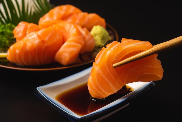Foto pauzinhos de comida japonesa sashimi salmon e wasabi na mesa preta