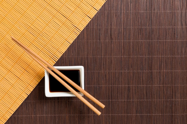 Foto pauzinhos e tigela com molho de soja em dois bambu esteira blak e amarelo vista superior com espaço de cópia