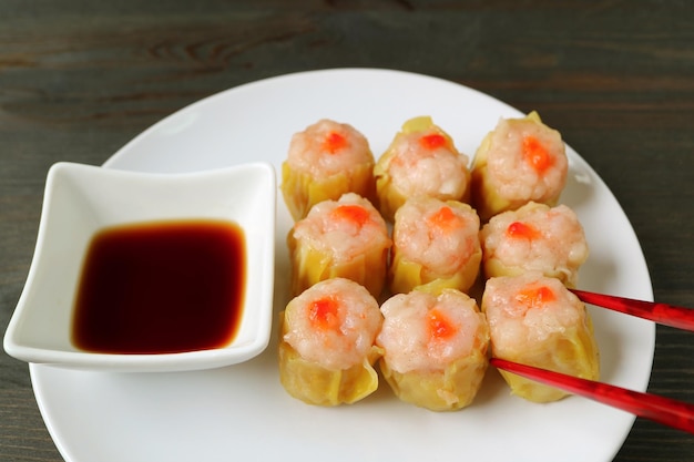 Pauzinhos vermelhos pegando um shumai ou camarão e carne de porco recheada com bolinho chinês cozido no vapor