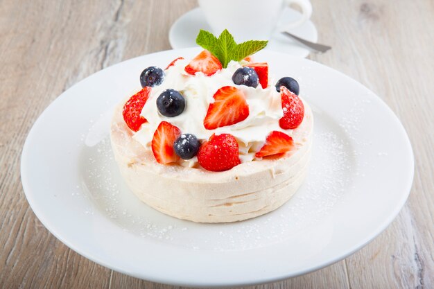 Pavlova-Dessert auf einem weißen Teller mit einer Tasse