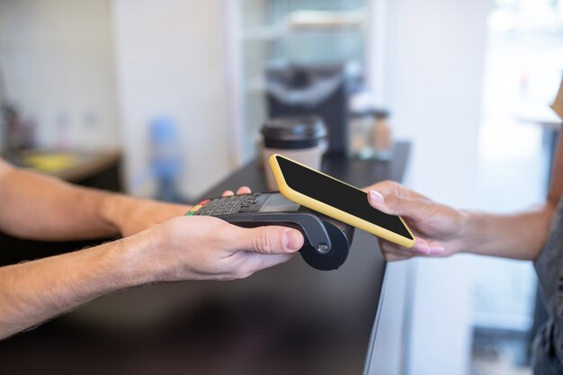 Pay Pass. Männliche Hände halten schwarz pos Terminal und weiblich bringt Smartphone, Gesichter sind nicht sichtbar