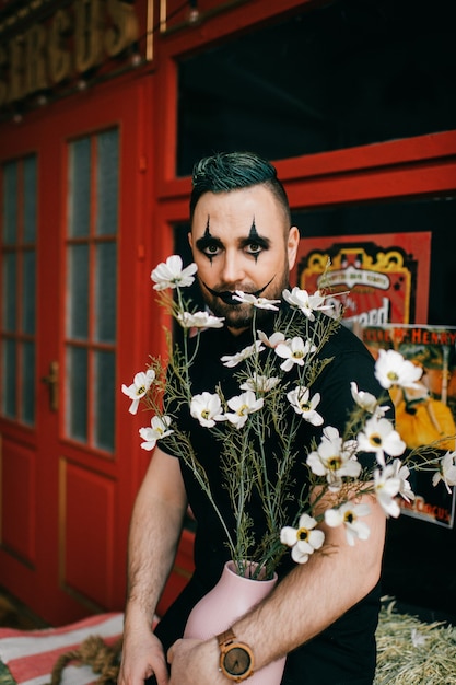 Un payaso gótico negro posando con flores.