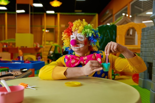 Un payaso gracioso jugando con un juego de té de juguete en la sala de juegos de niños.