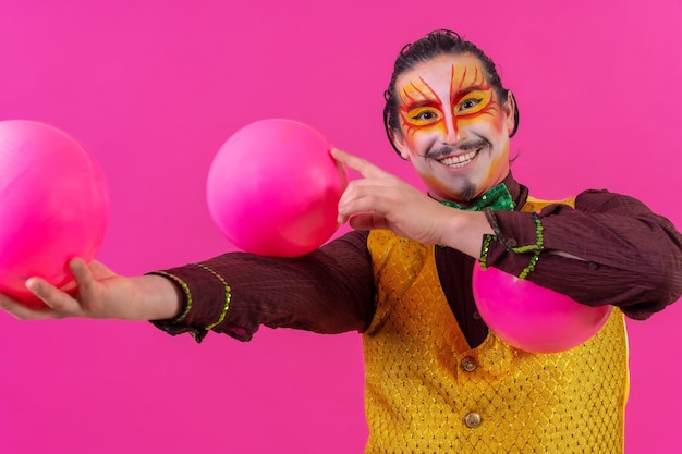 Payaso con maquillaje facial blanco sobre fondo rosa haciendo malabares con bolas