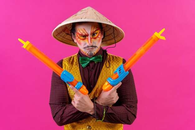 Payaso con maquillaje facial blanco sobre un fondo rosa con pistolas de juguete