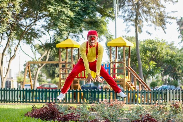 Payaso sonríe mientras salta en un parque pantalones rojos camisa amarilla