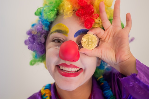 Payaso sonriente sosteniendo una moneda de Bitcoin en la dirección de sus ojos