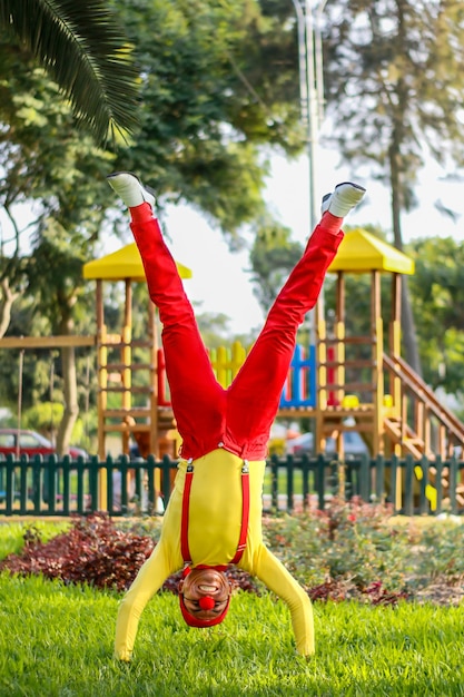 Foto payaso se para en sus manos con las piernas abiertas en un parque