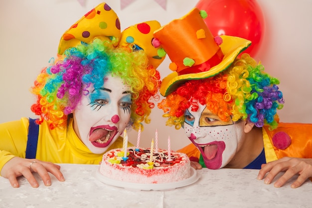 Payasos emocionales felices en la fiesta tratando de comer el pastel de cumpleaños