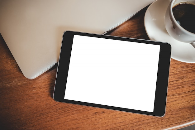 Pc tablet preto com tela branca de mesa em branco com laptop e xícara de café na mesa de madeira