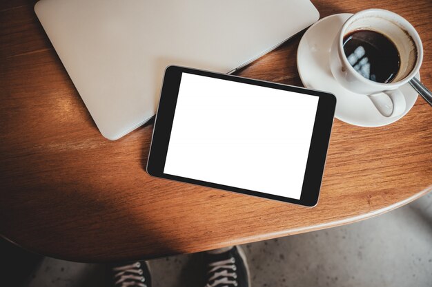 Pc tablet preto com tela branca de mesa em branco com laptop e xícara de café na mesa de madeira