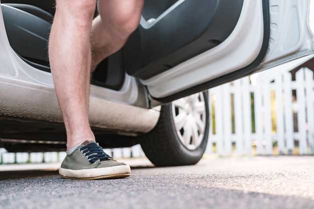 Pé masculino vestido com um tênis perto de um carro estacionado em uma rua de uma cidade provincial ha contra cerca