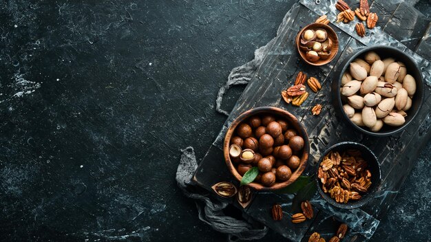 Pecanas exóticas y nueces de macadamia en tazones sobre fondo de piedra negra Vista superior Espacio libre para su texto