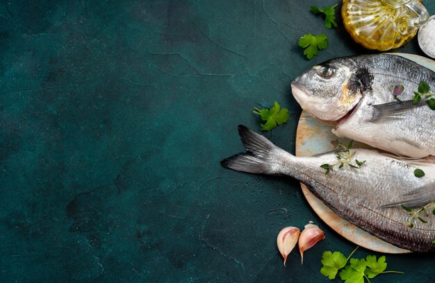 Peces dorados crudos e ingredientes sobre fondo turquesa de moda con un espacio para un texto