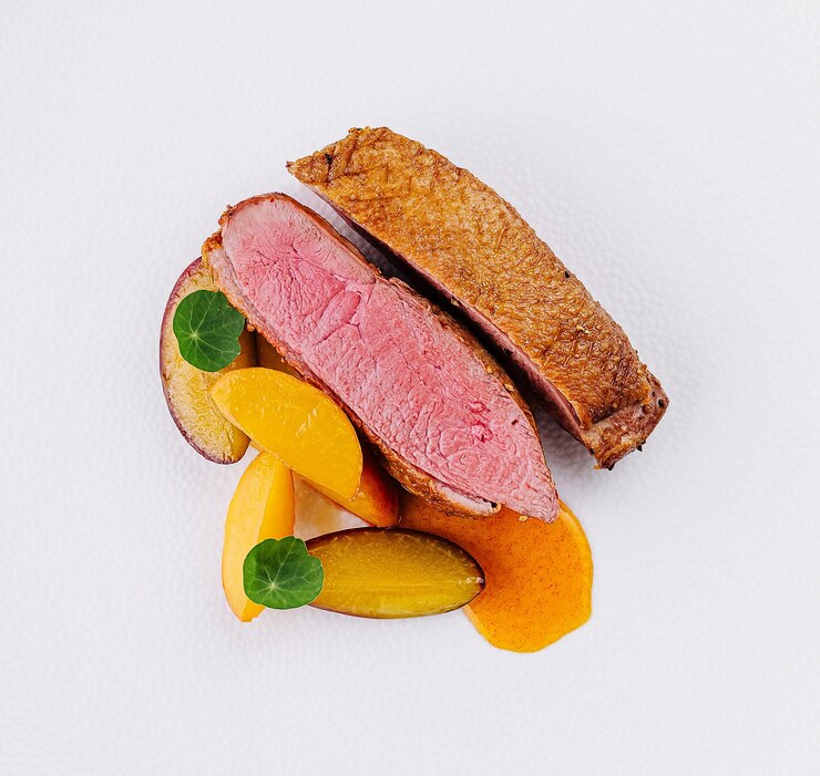 Pecho de pato gourmet con rebanadas de melocotón en un plato blanco