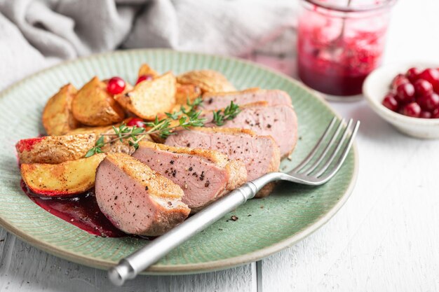 Foto pecho de pato con patatas y salsa de bayas en fondo blanco enfoque selectivo