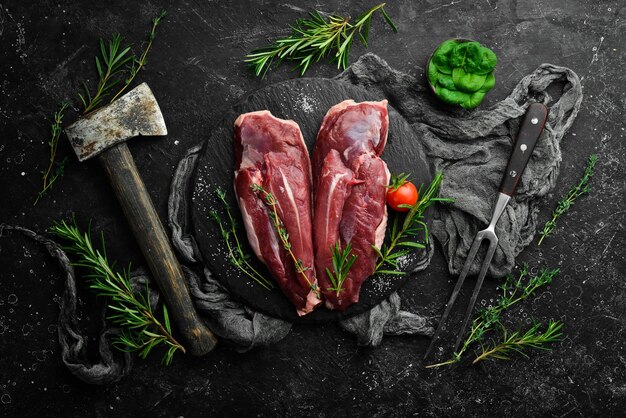 Pechuga de pato cruda con verduras frescas y especias en una tabla de cortar sobre un fondo negro Vista superior