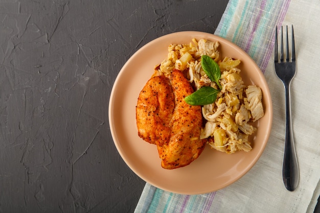 Foto pechuga de pollo al horno con ensalada en un plato decorado con espinacas junto a un tenedor sobre un fondo de hormigón