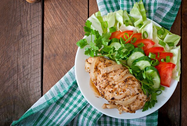 Pechuga de pollo al horno y verduras frescas en el plato sobre un fondo de madera