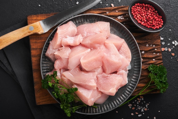 Pechuga de pollo cruda en rodajas o trozos cortados en tabla de cortar de madera con hierbas y especias sobre fondo de hormigón de piedra de pizarra oscura Carne de pollo cruda Vista superior con espacio de copia Maqueta