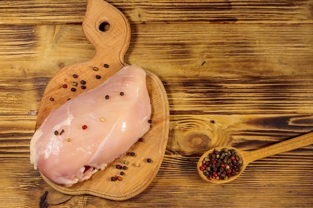 Pechuga de pollo cruda en tabla de cortar sobre mesa de madera