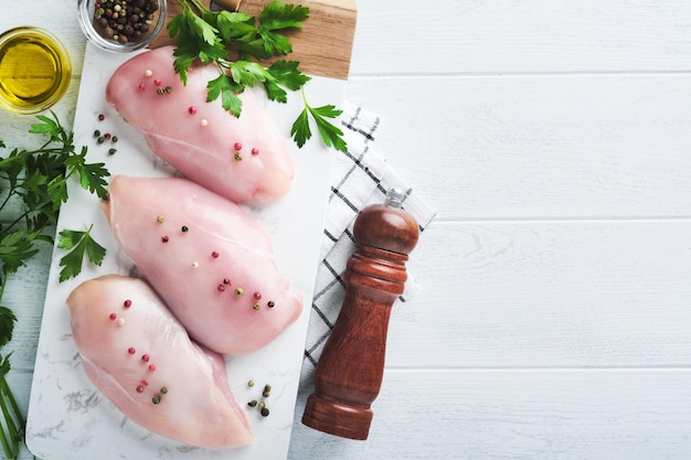 Pechuga de pollo Dos filetes de pollo con especias aceite de oliva y perejil en tabla de cortar de piedra blanca sobre fondo de mesa de madera blanca Vista superior con espacio de copia Fondo de cocina de carne de alimentos