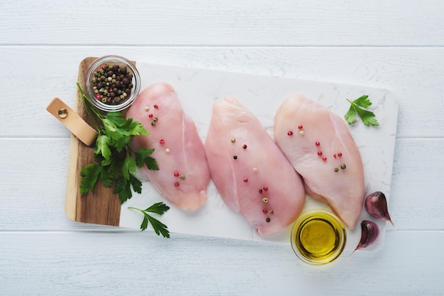 Pechuga de pollo Dos filetes de pollo con especias aceite de oliva y perejil en tabla de cortar de piedra blanca sobre fondo de mesa de madera blanca Vista superior con espacio de copia Fondo de cocina de carne de alimentos