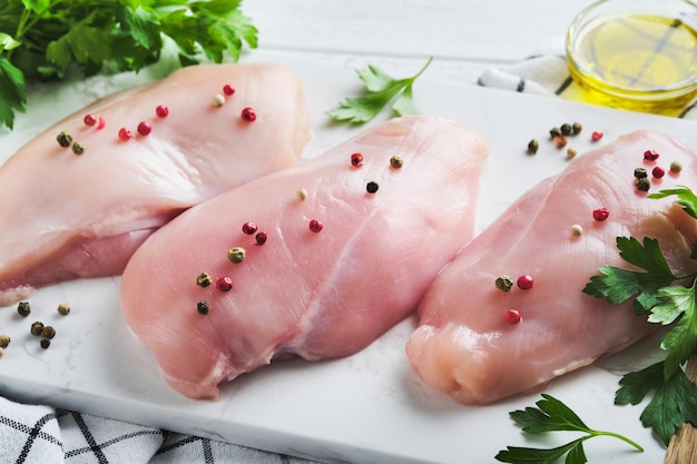 Pechuga de pollo Dos filetes de pollo con especias aceite de oliva y perejil en tabla de cortar de piedra blanca sobre fondo de mesa de madera blanca Vista superior con espacio de copia Fondo de cocina de carne de alimentos