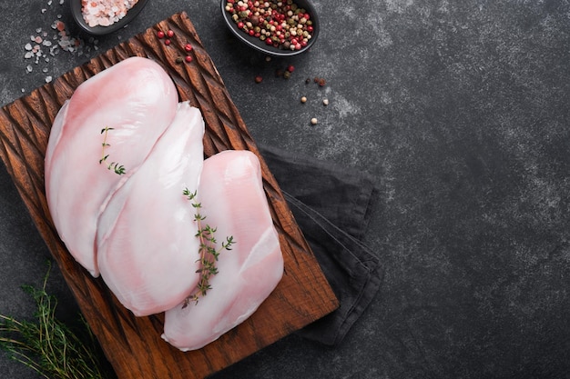 Pechuga de pollo Filetes de pechuga de pollo cruda en tabla de cortar de madera con hierbas y especias sobre fondo negro Vista superior con espacio de copia