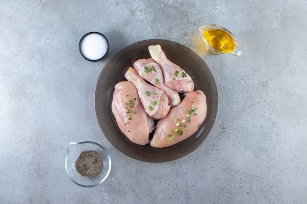 Pechuga de pollo y muslos en un plato junto a cuencos de especias, sobre la superficie de mármol.