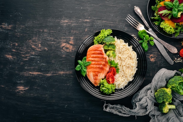 Pechuga de pollo a la parrilla con arroz y verduras Comida saludable En una mesa de madera negra Vista superior Espacio libre para texto