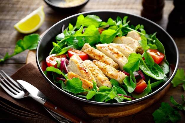 Pechuga de pollo a la parrilla y ensalada Ensalada de verduras frescas con espinacas de rúcula de tomate y carne de pollo a la parrilla en un tazón de comida saludable