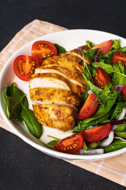 Pechuga de pollo a la parrilla con ensalada verde de ensalada de verduras frescas de lechuga, rúcula, espinacas, pepino y tomate en el plato sobre mesa gris. Menú de almuerzo saludable. Fondo de alimentos dietéticos. Vista superior