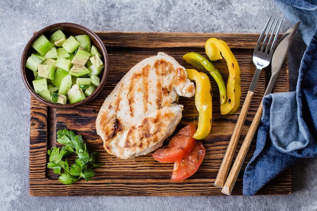 Pechuga de pollo a la parrilla con salsa de tomate y pimiento y salsa de aguacate sobre tabla de madera