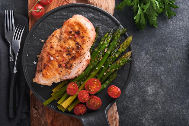 Pechuga de pollo a la parrilla con verduras Filete de pollo a la parrilla espárragos y tomates cherry en plato negro sobre fondo de mesa de hormigón gris Almuerzo de dieta saludable Filete de barbacoa frito Vista superior