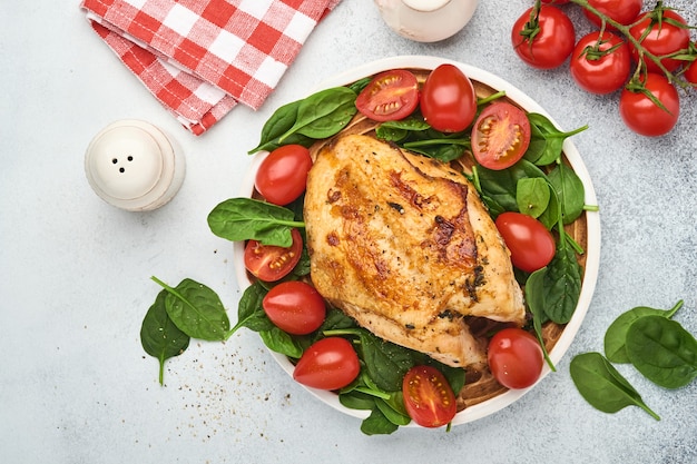 Pechuga de pollo a la plancha con ensalada de espinacas, pimiento y tomates cherry en un plato de cerámica en el fondo de la mesa blanca. Comida sana, dieta cetogénica, concepto de almuerzo. Vista superior y espacio de copia