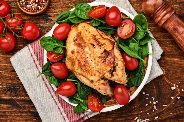 Pechuga de pollo a la plancha con ensalada de espinacas, pimiento y tomates cherry en un plato de cerámica sobre un fondo de mesa de madera vieja. Vista superior.