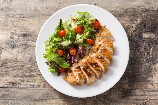 Pechuga de pollo a la plancha con verduras en un plato sobre la mesa de madera. Vista superior.