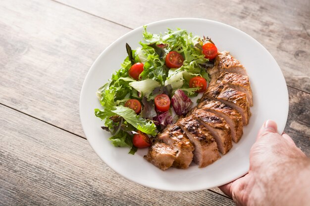 Pechuga de pollo a la plancha con verduras en un plato sobre la mesa de madera.