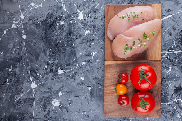 Pechuga de pollo y tomates en una tabla, en el azul.