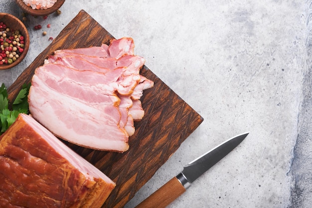 Pechuga de tocino de losa ahumada entera Jamón ahumado en rodajas sobre una mesa de madera con sal de pimienta de perejil de romero y ajo sobre fondo de mesa de hormigón gris antiguo Espacio de copia