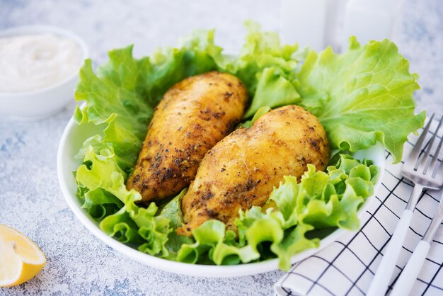 Pechugas de pollo al horno en especias y aceite con hierbas frescas para la cena, comida sana sobre un fondo claro, enfoque selectivo