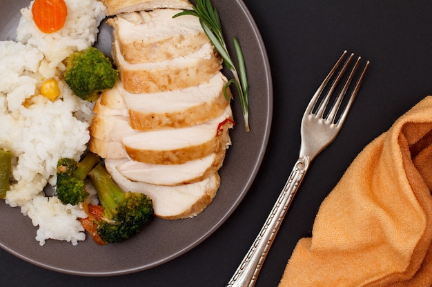 Pechugas de pollo al horno o filete con arroz, verduras y verduras en un plato con tenedor y servilleta. Vista superior.