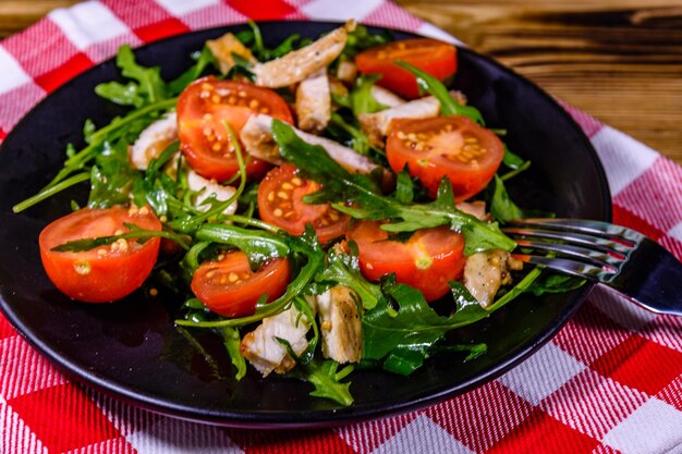 Pechugas de pollo asadas y ensalada con rúcula y tomates cherry en una placa negra