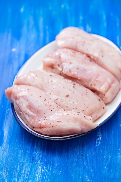 Foto pechugas de pollo crudas en plato blanco sobre superficie de madera azul