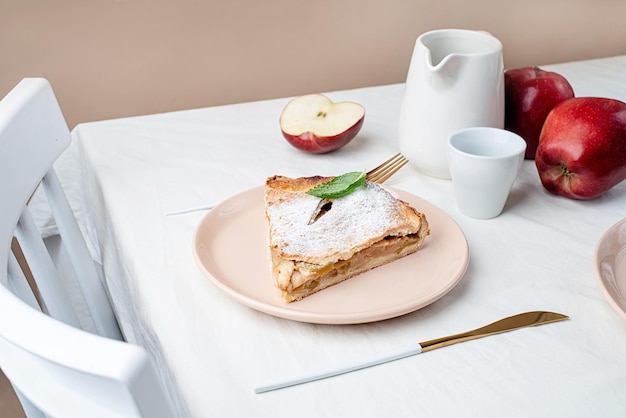 Pedaço caseiro de torta de maçã com maçãs vermelhas frescas na mesa branca