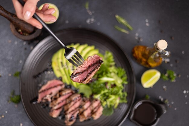 Foto pedaço cozido de filé de atum grelhado com fatias de abacate e salada em prato de cerâmica preta