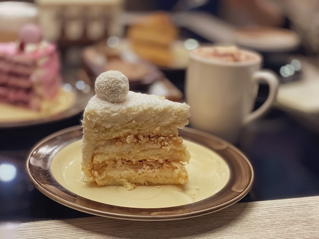 Foto pedaço de bolo branco com pão de ló, flocos de coco e decoração em cima do bolo em forma de bola em um prato em um restaurante.