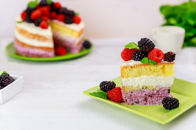 Pedaço de bolo de baga decorado com framboesas frescas e amoras na mesa branca.